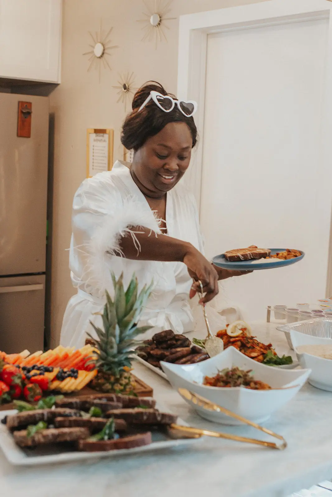 Guest in a feathered robe serving herself from a HumbledHandz brunch spread with a pineapple fruit display
